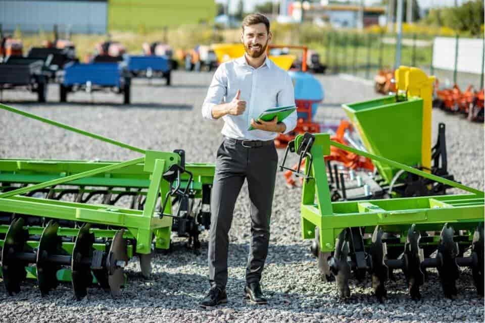 photo of a smiling machinery salesman standing surrounded by farm equipment